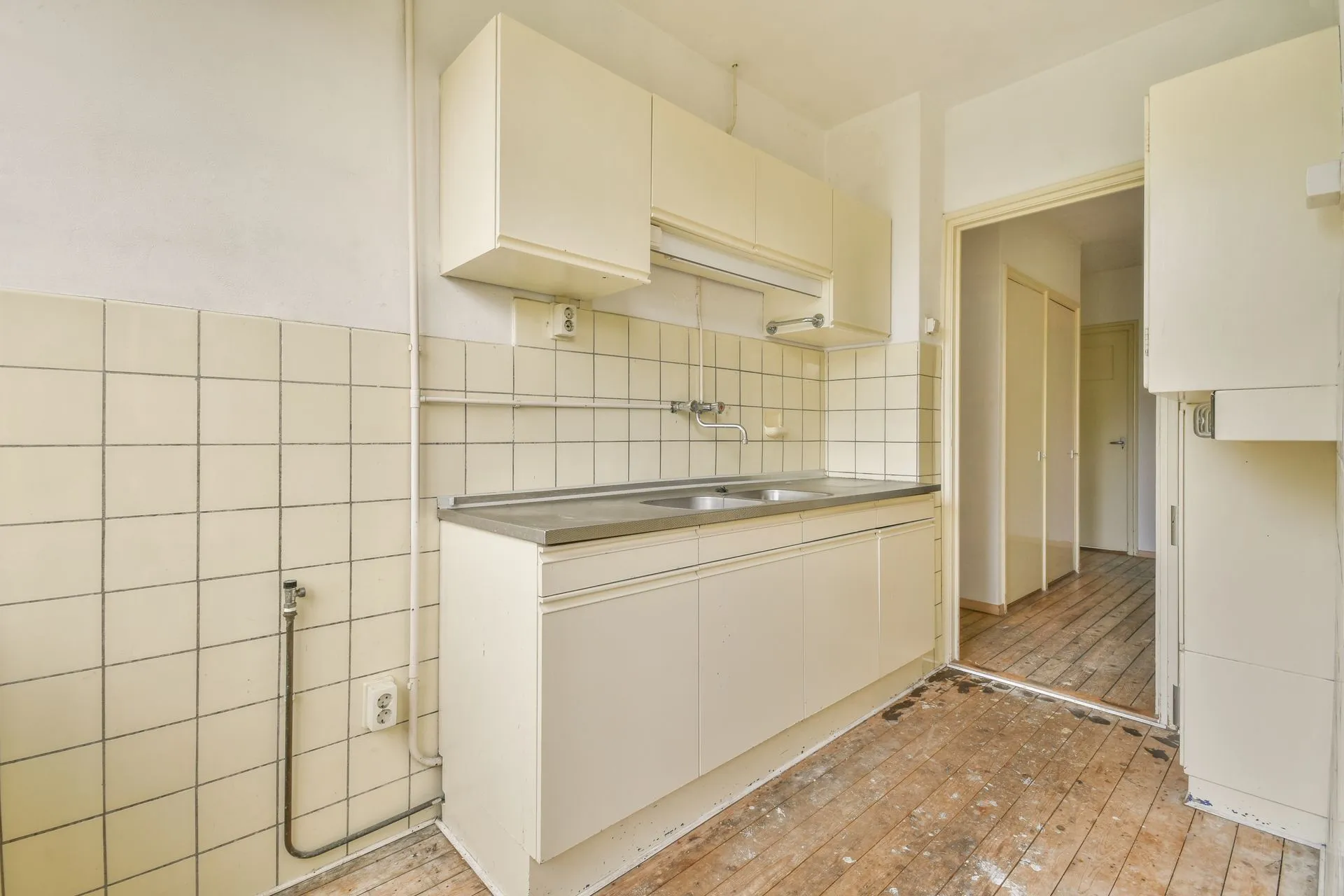 An empty kitchen with white cabinets and a wooden floor.